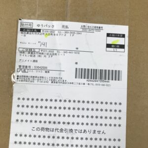 Cardboard box with a white delivery label containing Japanese text, an address, and a barcode sticker visible on the lower portion of the label.