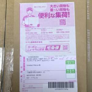 Pink Japanese delivery label affixed to a cardboard box, featuring a courier illustration, large Japanese text, a QR code, barcode, and shipping details.