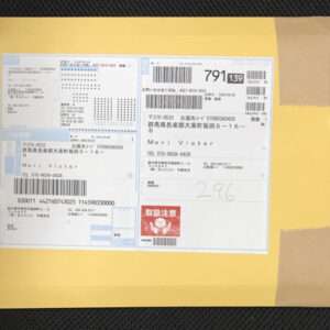 Yellow padded envelope with several shipping labels and barcodes, featuring Japanese text and a red handling sticker.