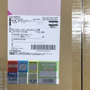 Cardboard box with a white shipping label featuring a barcode and Japanese address details; colorful color-code stickers at the bottom edge.
