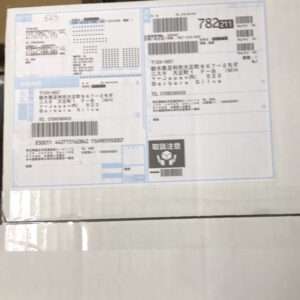 Box with multiple shipping labels and barcodes, mostly Japanese text on a white surface