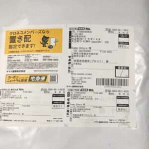 Japanese delivery label on a white envelope with a yellow promotional panel featuring a cat mascot; right side shows sender/recipient details and barcodes, typical courier paperwork.