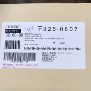 A Japanese shipping label on a light envelope with barcodes, postal code 〒326-0807 and various Japanese text fields.