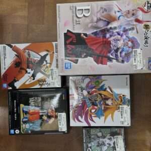 Assorted boxed anime action figures laid out on a wooden floor, featuring colorful character art and branding from Bandai and Konami.