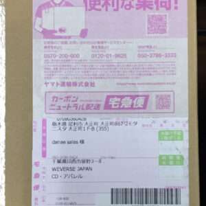 Cardboard box with a pink shipping label showing a cartoon courier, large Japanese text, and a barcode