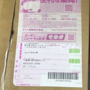 Front of a cardboard parcel with a pink Yamato Transport 'Ta-Q-Bin' shipping label, showing recipient/address fields, a barcode, and tracking numbers.