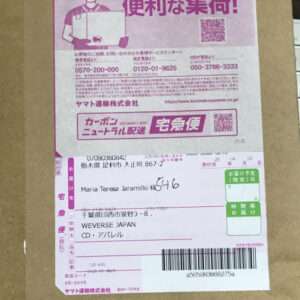 Cardboard box with a pink shipping label featuring a worker illustration, Japanese text, and a barcode for tracking and delivery details.