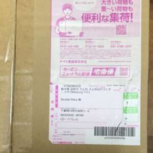 Brown cardboard box with a large pink Japanese delivery label featuring a courier illustration and barcode, indicating a shipped package