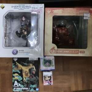 Boxed anime figures on a wooden floor: Sword Art Online’s Yuuki figure in a white box on the left, a large orange-box figure on the right, with a My Hero Academia figure and two small boxed figures at the bottom center/bottom left.
