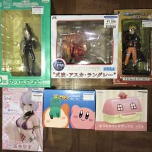 Shelf of boxed anime figures in colorful packaging with clear plastic windows showing characters like Naruto and Kirby-style faces, Japanese text on boxes