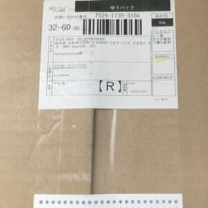White shipping label with a barcode and Japanese text attached to a brown cardboard box; includes a tracking number and other shipping details.