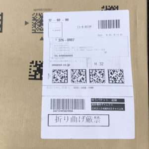 Cardboard box with a white shipping label featuring barcodes, QR codes, and Japanese text.