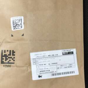 Brown cardboard box with a white shipping label showing a QR code and barcodes on the front edge of the package.