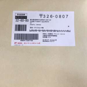 White shipping label with barcode and Japanese text affixed to a brown envelope, showing tracking numbers and address blocks in small print.