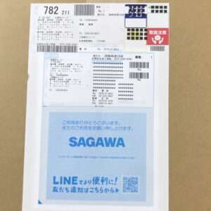 Package with a shipping label and a blue SAGAWA notice on a cardboard box, showing Japanese text and a QR code area.