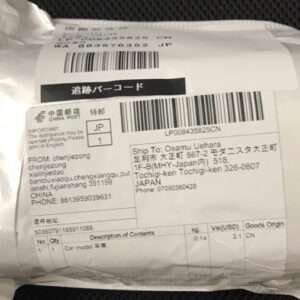 Padded white shipping envelope with a large barcode label, tracking numbers, and Japanese/Chinese text; shows destination and contents related to a car model.