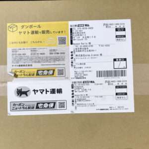 Cardboard box with multiple Japanese shipping labels and stickers, including the Yamato Transport logo and a yellow label with QR code and barcodes.