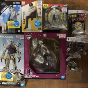 Collection of boxed Japanese action figures and model kits spread on a wooden floor, including a purple D figure box and a large white-and-blue Gundam box.