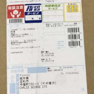 Japanese shipping label on cardboard with multiple barcodes and stamps, showing sender and recipient addresses, tracking numbers, and service icons.