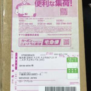 Shipping label on a cardboard box with a pink header, Japanese text, and a barcode; includes sender and recipient fields and tracking numbers.