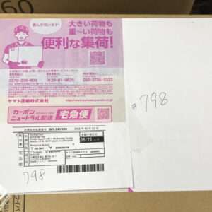 Box with a pink Japanese promotional label and a shipping label with a barcode on the side; handwritten '#798' on the box edge.
