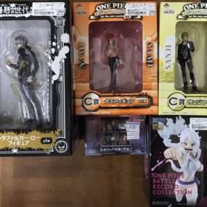 Display of four One Piece figures in boxes on a wooden floor: Trafalgar Law in a black box on the left, Nami in an orange box in the center, Sanji in a yellow box on the right, and a Battle Record Collection figure in a dark box at the bottom right.