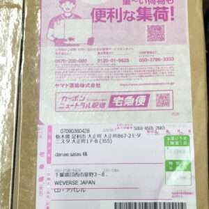 Pink Japanese delivery label on a brown cardboard box, showing addresses, a barcode, QR code, and service stamps for宅急便/配送.