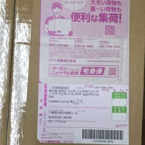 Pink Japanese shipping label on a cardboard box, featuring a cartoon courier, QR codes, and tracking barcodes.