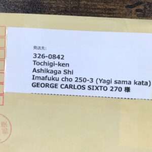 Close-up of a light-yellow envelope with a white label showing a Japanese mailing address (postal code 326-0842, Tochigi-ken, Ashikaga Shi, Imafuku cho 250-3) and the recipient name GEORGE CARLOS SIXTO 270 様.