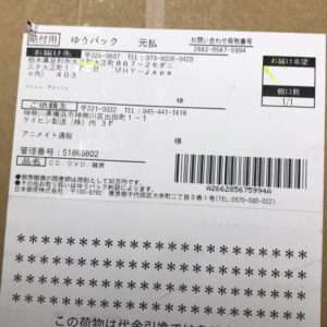 Japanese shipping label on a brown package with a barcode, multiple address fields, and small print text in Japanese.