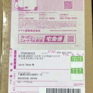 Pink-and-white shipping label on a cardboard box, showing recipient and sender info in Japanese, a barcode, and two QR codes.
