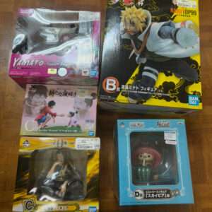 Boxed anime figures laid out on a wooden floor, including a large Naruto figure box and several One Piece figures in pink, yellow, and blue packaging.