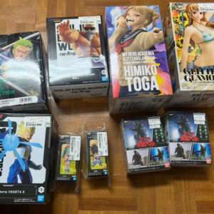 A collection of boxed anime figures laid out on a wooden floor, featuring characters from One Piece, Dragon Ball, and My Hero Academia.",