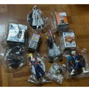 Collection of assorted anime figurine figures in plastic bags laid on a wooden floor, with boxed figures in the mix.