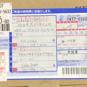 A Japanese parcel with multiple labels and handwritten address fields on a blue wrap, showing sender and recipient details and tracking numbers.