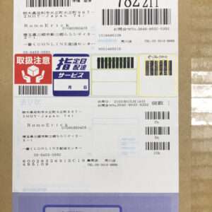 Front of a cardboard parcel with multiple Japanese shipping labels, barcodes, and service stamps; addresses and tracking numbers are visible.