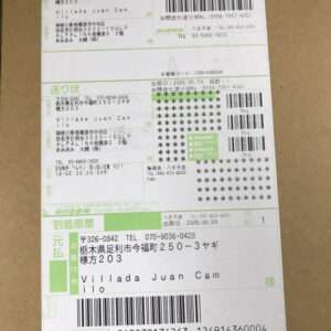 Shipping label on a brown cardboard box with multiple barcodes, tracking numbers, and sender/recipient details in Japanese and English.