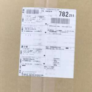 Cardboard box with a large white shipping label showing barcodes and Japanese text, including tracking fields.