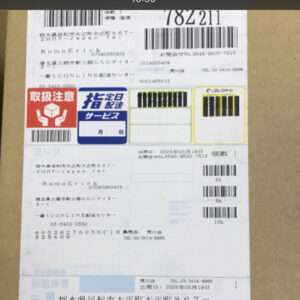 Shipping label on cardboard with multiple barcodes, Japanese text, and red and blue service icons.