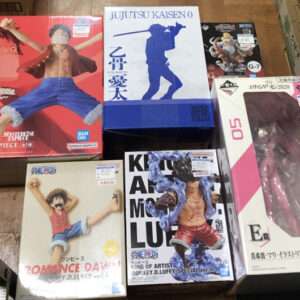 Collage of boxed anime figures on a wooden floor, including One Piece and Jujutsu Kaisen collectibles from Bandai.