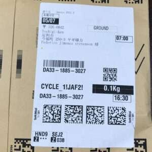 Parcel with a white shipping label showing destination, date, time, weight 0.1 kg, and multiple barcodes on a brown box with a yellow CX32 sticker.