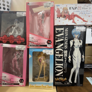 Display of multiple Evangelion action figure boxes on a shelf, featuring Shikinami Asuka Langley and Mari Illustrious figures in pink packaging and a large Neon Genesis Evangelion box with a blue-haired figure.