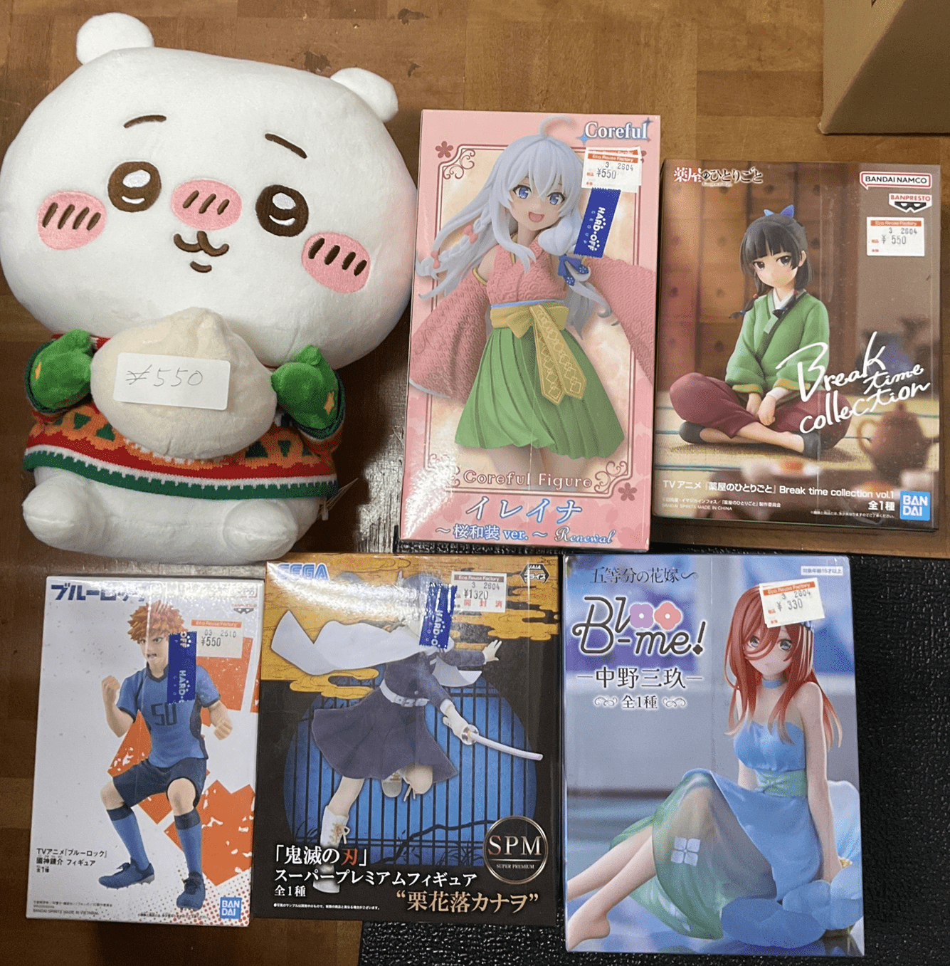 Ver Fotos Recientes 102 - Articulos Japan (post Box Japan) Plush white bear with pink cheeks and a price tag sits beside boxed anime figures on a wooden floor. Articulos Japan (Post Box Japan)