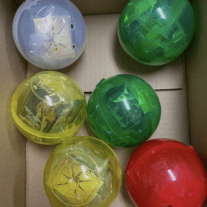 Six translucent plastic capsules in a cardboard box: blue, yellow, green, and red pods arranged in a grid of three by two.