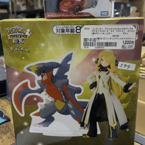 Boxed Pokémon Masters EX panel spectacle figure set featuring a blue dragon-like Pokémon and a blonde female character in a white and gold outfit; price tags visible in Japanese store.  Articulos Japan (Post Box Japan)