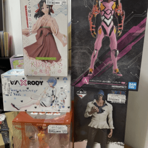 Stack of boxed anime figures on a shelf, including a large pink Evangelion model on the right and a character in a pink kimono on the left.