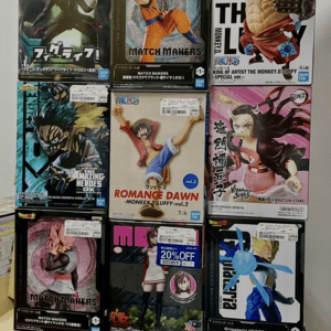 Stacked boxes of anime figurines on a table, featuring characters from Dragon Ball, One Piece, and more, arranged into a tall tower against a wall.