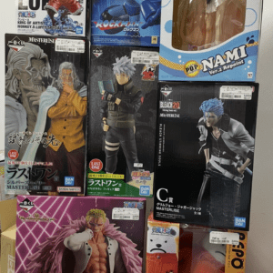 Pile of boxed anime figures on a display shelf, featuring Mega Man, Nami, Luffy, and other characters in colorful packaging with price stickers.