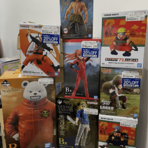 Stack of boxed Naruto action figure boxes on a display shelf, featuring characters in colorful outfits and a large orange-suited figure at the front left.