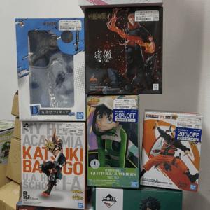 Stack of anime figure boxes stacked in a tower against a wall, featuring Kirby on top and My Hero Academia figures in the middle and bottom rows, with colorful packaging.